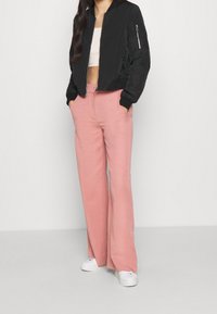 Veste bomber noire avec poche zippée, associée à un pantalon large taille haute rose clair et des baskets blanches.