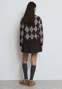 Suéter de punto argyle en granate y gris, falda negra plisada, calcetas grises hasta la rodilla y botines marrones con un adorno decorativo.