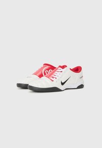 Baskets Nike avec une tige en cuir blanc, des accents rouges, des détails noirs et une semelle texturée pour l'adhérence.