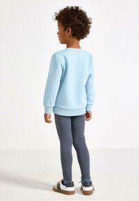 Light blue sweatshirt with long sleeves, paired with dark gray leggings and white sneakers featuring black accents. Simple design, no patterns.