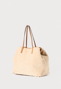 Beige faux fur tote bag med brune læderremme. Blød tekstur og rund form, med et rummeligt interiør uden synlige beslag.