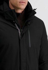 Zwarte waterdichte jas met hoge kraag, rits aan de voorkant en donkere accenten. Beschikt over een ritszak en een gestructureerde binnenvoering.