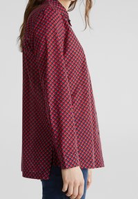 Camicia rossa a maniche lunghe con un motivo circolare in tonalità di rosso e blu. Presenta un colletto con bottoni e una vestibilità dritta.