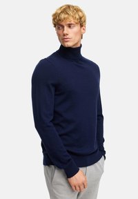 Marineblauer Rollkragenpullover aus weichem Stoff, mit schmaler Passform und gerippten Bündchen. Kombiniert mit hellgrauen Jogginghosen für einen lässigen Look.