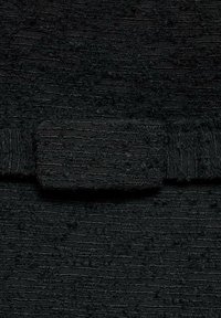 Črn teksturiran material z izbočenim vzorcem, ki vsebuje pravokotni pas ali oblogo iz podobnega materiala za poudarjanje.