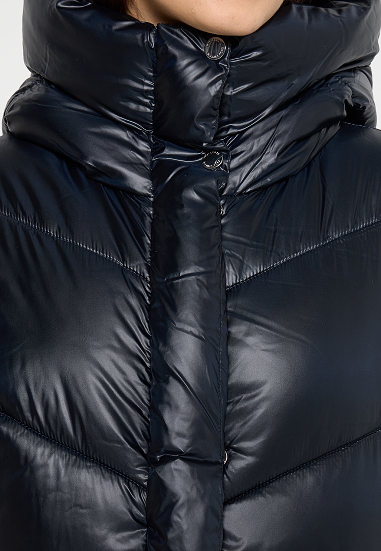 Doudoune bleu marine avec un col haut, finition brillante et fermeture à boutons. Présente des coutures diagonales et une texture matelassée.