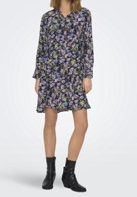 Abito a maniche lunghe con stampa floreale in tessuto scuro, con accenti viola, blu e giallo; colletto con bottoni; orlo arricciato; lunghezza al ginocchio. Stivaletti neri alla caviglia.