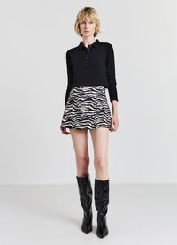 Polo a maniche lunghe nero, in misto cotone, con pattina a bottoni. Gonna mini a stampa zebra, design svasato. Stivali neri in pelle al ginocchio, punte a punta.