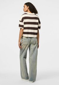 Pull court rayé en crème et marron, avec un col et de larges manches courtes. Porté avec un jean taille haute bleu clair.