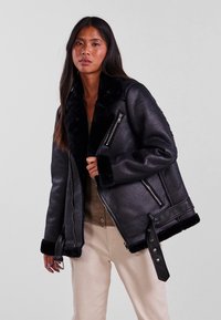 Black leather shearling jacket with a wide collar, zippered pockets, and snap-button accents. Soft texture with contrast shearling trim.