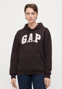 Hanorac maro cu șnururi și un buzunar frontal, având un logo brodat alb "G.A.P.". Material moale cu o croială ușor lejeră.