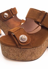 Sandali con zeppa in suede marrone, dotati di una piattaforma in sughero, cinturino regolabile e un dettaglio decorativo con bottone e perla.