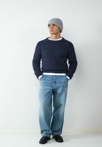 Granatowy sweter dzianinowy z okrągłym dekoltem, noszony na białej koszuli. Jasnoniebieskie luźne dżinsy i szary beret dopełniają całość. Czarne buty.