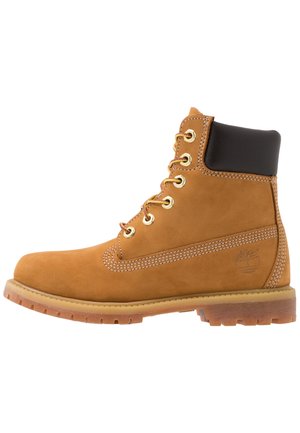 Botte de travail en cuir marron clair avec col noir rembourré, œillets dorés, lacets jaune-brun, semelle épaisse et logo arbre Timberland sur le talon.
