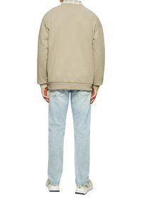 Felpa beige con vestibilità comoda, polsini a coste, abbinata a jeans in denim blu chiaro. Dettaglio del colletto a quadri visibile e calzature casual.
