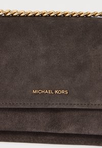 Pilkos zomšos rankinė su auksine grandine, su auksiniu logotipu "MICHAEL KORS" ir lygiu, tekstūriniu paviršiumi.