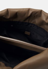 Intérieur d'un sac en cuir marron avec doublure en tissu noir, doté d'une poche zippée et d'un détail zippé en argent sur le bord supérieur. Matière douce et texturée.