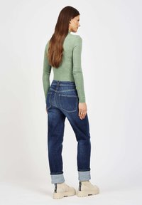 Long-sleeve green top, dark wash cuffed denim jeans, beige platform boots with black accents, and visible back pockets.