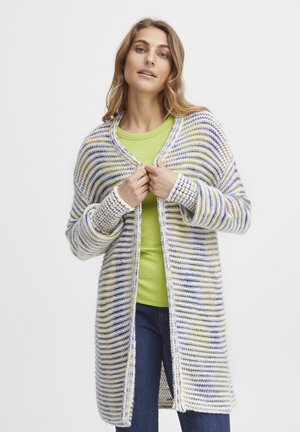 Cardigan long rayé en blanc, vert et violet, avec une coupe ample, une ouverture à l'avant et une texture côtelée. Porté par-dessus un haut vert et un jean bleu.