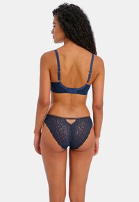 Navy blauwe kant bralette met verstelbare bandjes, voorzien van een textuur met bloemenpatroon. Bijpassende slip met een uitsnijding aan de achterkant.