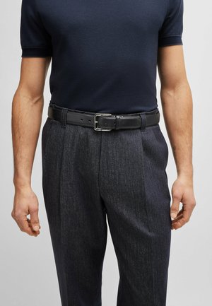 Navy short-sleeve polo shirt paired with dark gray textured trousers and a black leather belt featuring a silver buckle.
