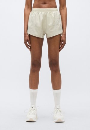 Pantaloni scurți atletici bej cu o talie elastică, având deschideri laterale și o textură subtilă de plasă. Asortați cu șosete albe până la genunchi și încălțăminte.