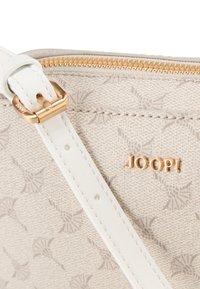 Beige mønstrede stof crossbody taske med hvid justerbar rem, guldkvadrat hardware og præget logo detalje. Lynlåslukket toprum.