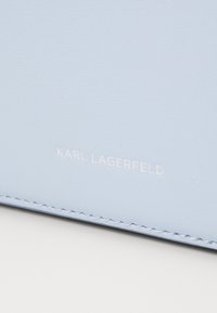 Ljusblått läderplånbok med slät textur, prydd med vit präglad varumärkesnamn "KARL LAGERFELD" och kontrasterande sömsdetaljer.