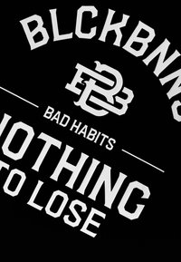 Zwarte stof met gedurfde witte letters. De tekst bevat "BLCKBNN" en "BAD HABITS" met grafische accenten die een sportieve uitstraling benadrukken.