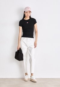 T-shirt nera aderente con piccolo logo, jeans bianchi strappati, sneakers platform beige e borsa nera a trama "bear", completato con un cappellino rosa.