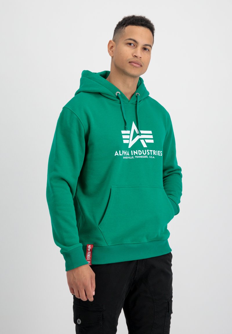 Sudadera verde hecha de una mezcla de algodón con un bolsillo frontal, capucha con cordón y logo blanco. Presenta puños acanalados y una etiqueta en el dobladillo.