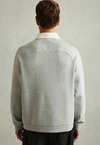 Sweatshirt gri deschis cu guler rotund, croială oversized și tiv ribant, având un guler alb contrastant și o textură netedă.