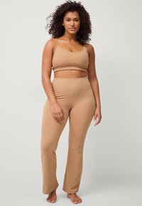 Beige træningssæt med en cropped top med tynde stropper og højlivede flared leggings, fremstillet af glat, strækbart stof.