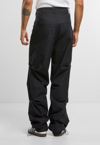 Zwarte cargo broek met een ontspannen pasvorm, voorzien van meerdere zakken, een aantrekkoord aan de onderrand en een stevige stoftextuur. Achteraanzicht weergegeven.