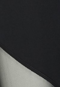 Svart tyg med en texturerad grå panel längs den nedre kurvan har kontrasterande sömmar; slät och matt yta med en stilren design.