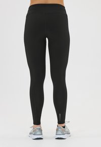 Schwarze Leggings mit einem hohen Bund, glatter Textur und dezenten Seitennähten. Kombiniert mit grauen Sportschuhen mit orangefarbenen Akzenten.