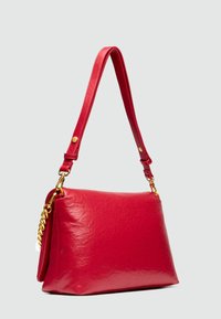 Sac à main en simili cuir rouge avec une texture lisse, un accent en chaîne dorée et une bandoulière réglable. Le sac a une forme rectangulaire.