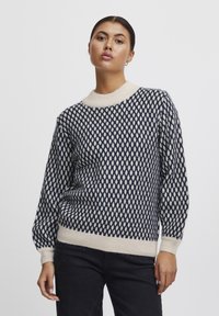 Maglione lavorato a maglia in navy e crema con un motivo a rombi, scollo a girocollo a costine e polsini. Texture morbida e vestibilità rilassata.