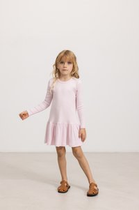Langermet rosa kjole med ribbet tekstur og svingende kant, kombinert med brune sandaler med stropper. Enkel, tettsittende boddesign.