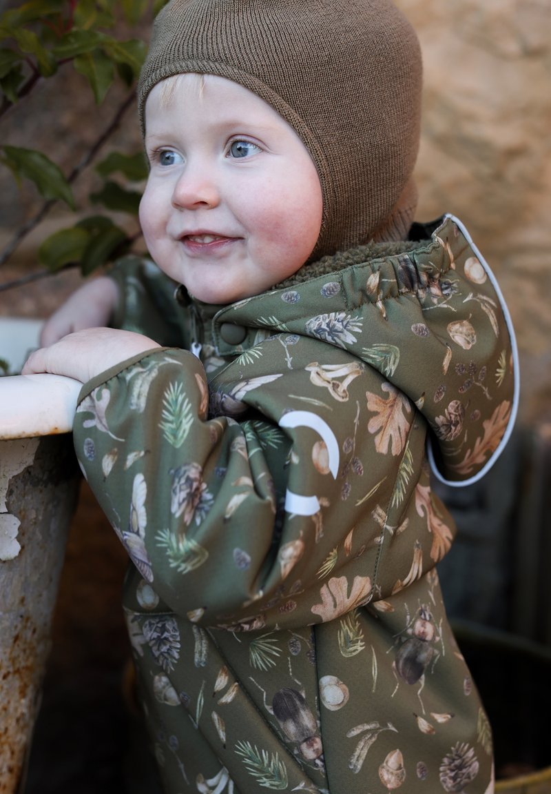 Zielona dziecięca kurtka z nadrukami o tematyce przyrodniczej, wyposażona w kaptur, zapinana na zamek błyskawiczny i posiadająca miękką podszewkę. Dziecko ma na głowie brązową dzianą czapkę.
