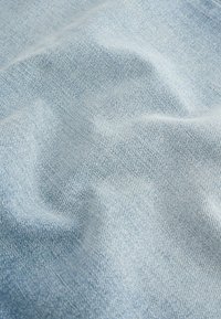 Tissu en denim bleu clair avec une surface légèrement texturée, présentant de fins motifs de tissage et de subtiles variations de teinte.