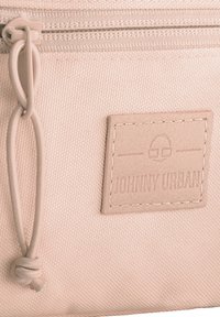 Jasnoróżowa torba materiałowa o teksturowanej powierzchni, z zamknięciem na zamek błyskawiczny i beżową skórzaną metką z wytłoczonym napisem "JOHNNY URBAN."