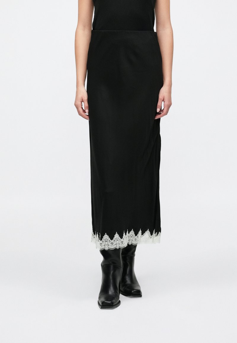 Jupe maxi noire à la texture lisse avec un bord en dentelle blanche à l'ourlet. Portée avec des bottines noires à talons pour créer un contraste.