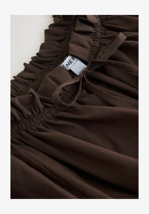 Smeđi materijal s nabranim volanom, s ušivenim elastičnim pojasom. Uključuje oznaku s natpisom "NEX." Glatka tekstura i jednobojna boja.