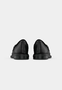Schwarze Lederschuhe mit flacher Sohle, schlankem Design, spitzem Zehenbereich und minimaler Naht. Mit goldfarbenen Hardware-Akzenten an der Seite.