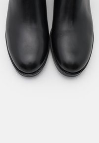 Bottines noires en cuir avec une finition lisse, bout arrondi et design minimaliste. Semelle plate et détails de couture discrets.