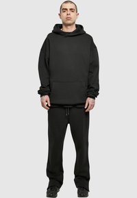 Felpa nera Oversize con tasca frontale e cordini, abbinata a pantaloni larghi coordinati e sneakers, realizzata in tessuto morbido.