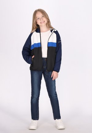 Vindjakke i marineblå, hvid og blå; har lynlås foran, løs pasform og to sidelommer. Sammen med mørke jeans og hvide sneakers.