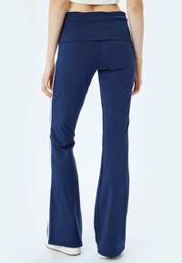 Marineblauwe flared workout broek van zachte stof, met een brede tailleband en witte zijkanten, met een gladde textuur en een getailleerd ontwerp.