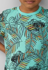 Korte mouw aquamarijn T-shirt met een palmbladpatroon in zwart en oranje, met geïllustreerde off-road voertuigen erin verwerkt.